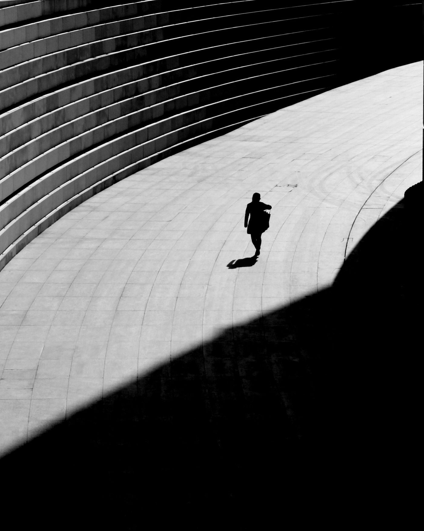 A lone silhouette crossing curved concrete steps in hard light